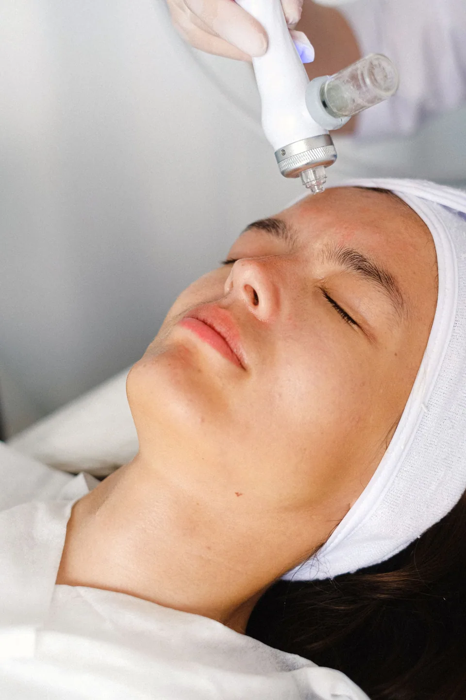 Clienta tumbada con turbante blanco y una boquilla de aparato facial sobre la frente