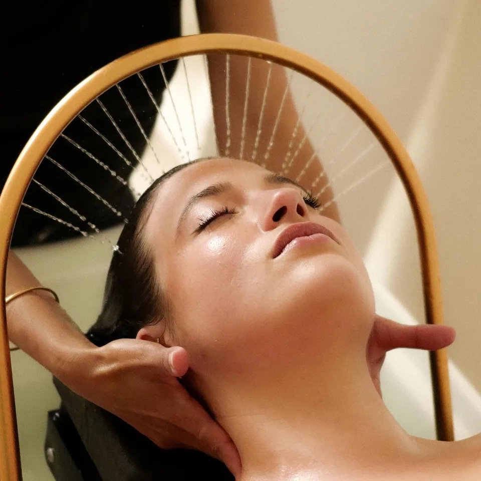 Client lying with eyes closed under a golden arch that lets fine streams of water fall on her hair