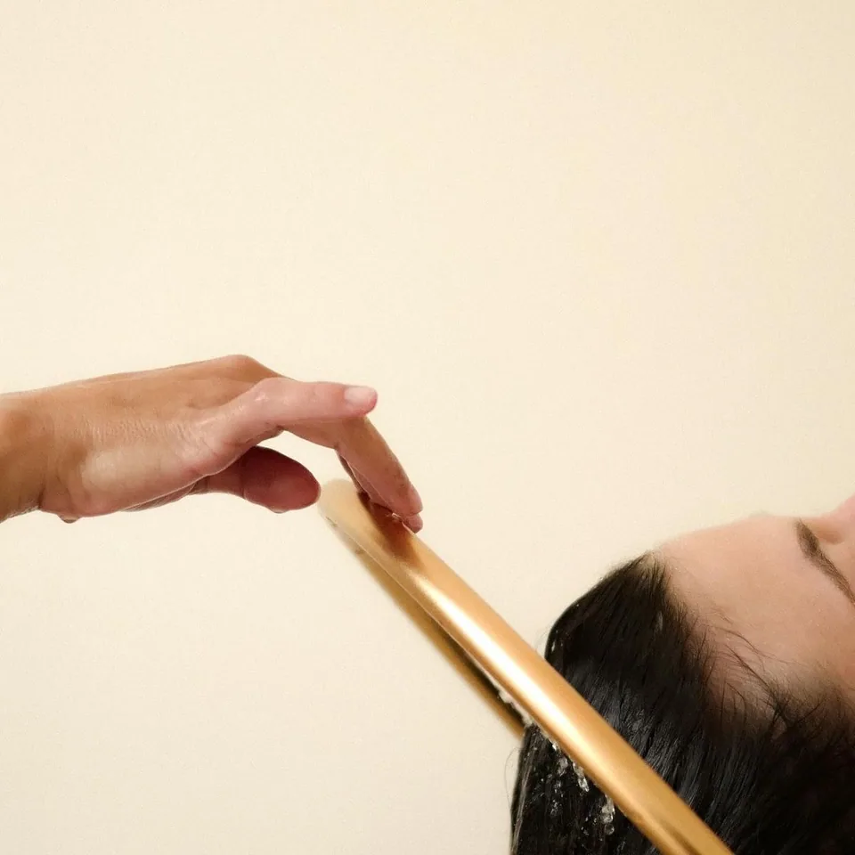 Main de la thérapeute sur l’arceau doré qui fait couler l’eau sur les cheveux